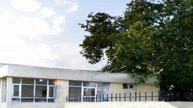 A modern building with a flat roof, large windows, and a central staircase.