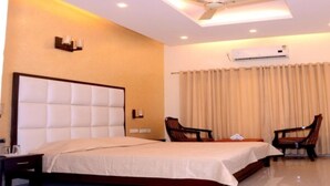 A hotel room with a large bed, two chairs, a desk, and an air conditioning unit.