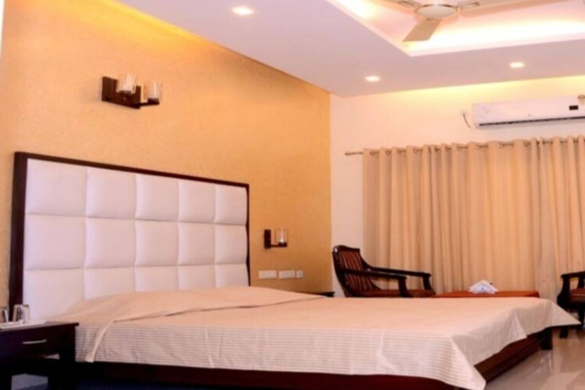 A hotel room with a large bed, two chairs, a desk, and an air conditioning unit.