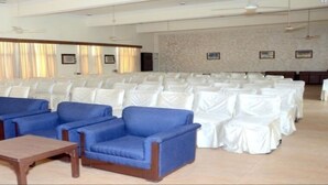A conference room with rows of white chairs, blue sofas, and wooden tables.