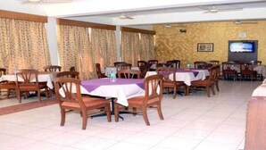 A restaurant with multiple tables and chairs, a television, and a 'NEXT' button on the wall.