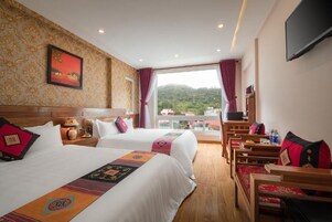 Habitación de hotel con dos camas, televisión, escritorio y vistas a las montañas.