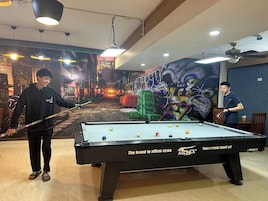 Una mesa de billar con un mural de fondo, un ventilador de techo y una mesa con sillas.
