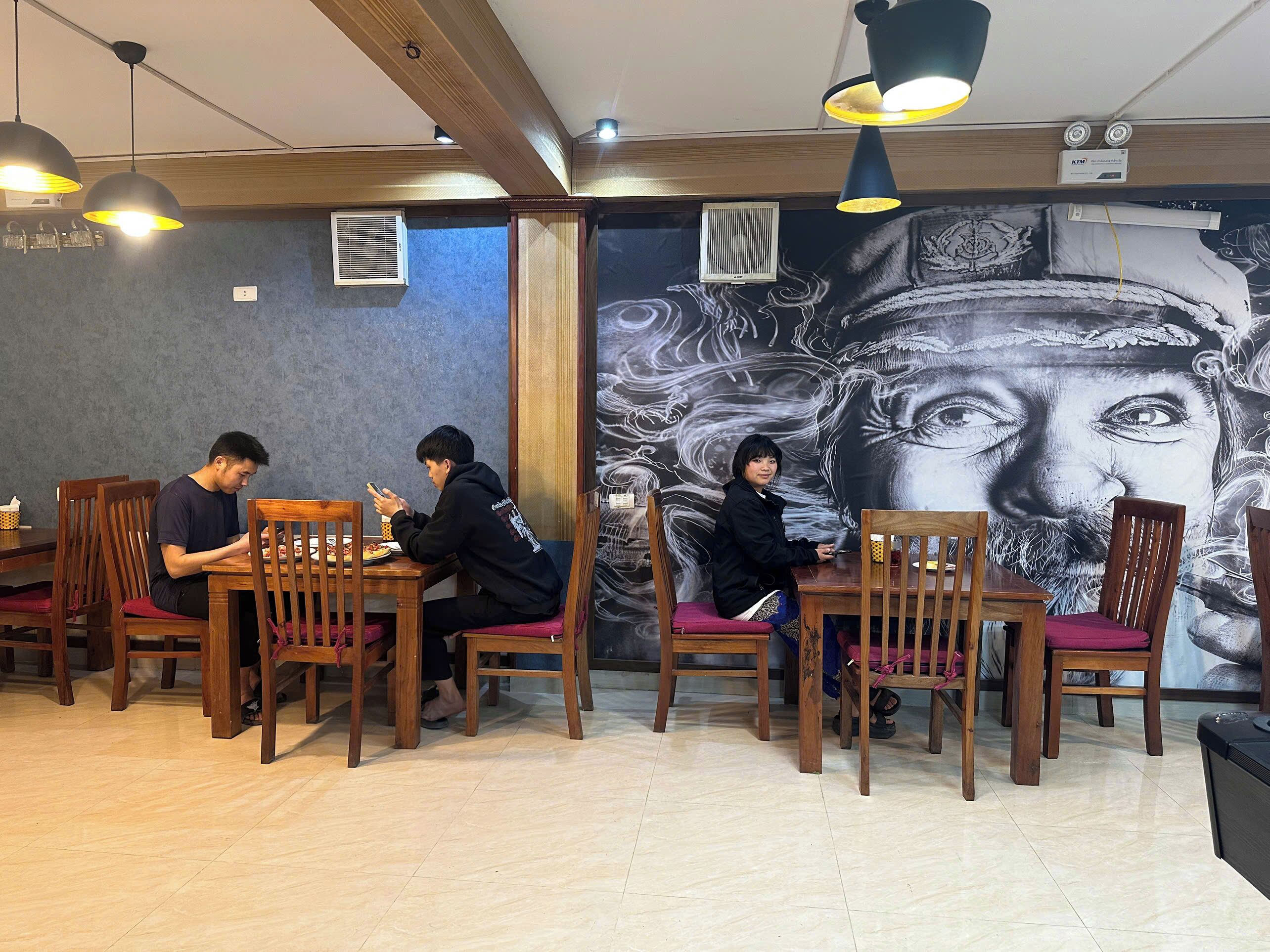 Un restaurante con mesas y sillas de madera, un mural en la pared e iluminación colgante.