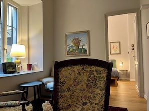 Una habitación con un sillón estampado con motivos florales, una mesita con lámpara y un cuadro en la pared.
