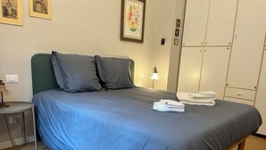 Un llit ben arropat amb roba de llit i coixins blaus, una taula de nit amb una làmpada i un armari amb diverses portes.