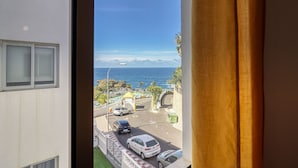 A view from a window overlooking a coastal street with parked cars and a clear blue sky.