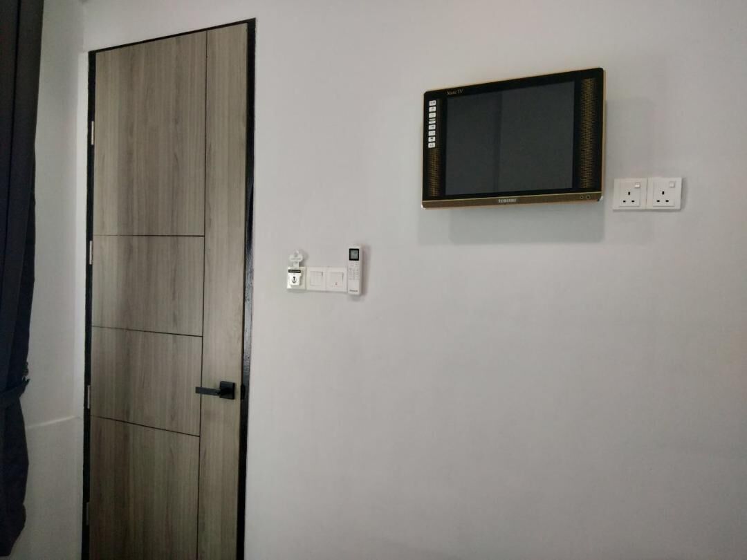 Una habitación con un armario de madera, un televisor de pantalla plana montado y un enchufe.