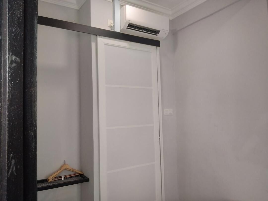 A room with a white door, a black-framed mirror, and a small shelf with a hanger.