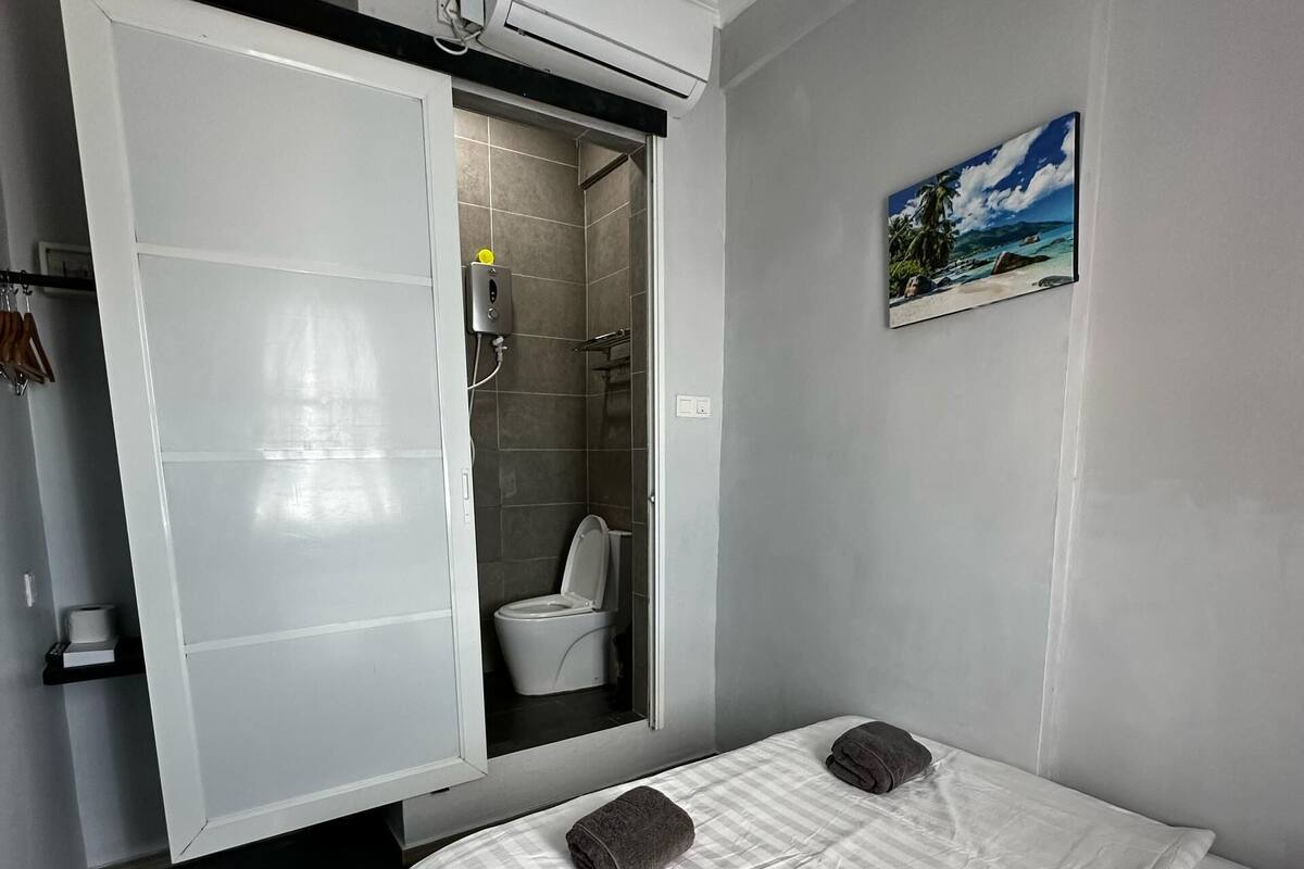Quarto de hotel pequeno com cama, chuveiro e vaso sanitário.