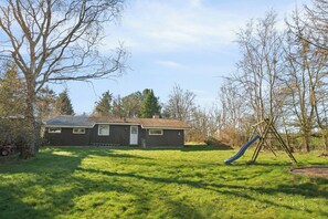 Une maison avec un jardin devant, une balançoire et un toboggan.