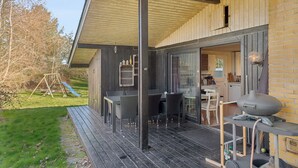 Ein überdachter Außenbereich mit Esstisch, Stühlen, einem Grill und einer Rutsche im Hintergrund.
