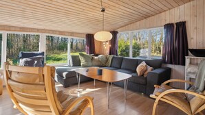Ein modernes Interieur mit Holzboden, großen Fenstern, einer Couch, einem Couchtisch und einem Sessel.