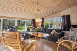 Ein modernes Interieur mit Holzboden, großen Fenstern, einer Couch, einem Couchtisch und einem Sessel.