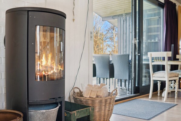 Un intérieur moderne avec un poêle à bois, un panier en osier et un coin repas avec des chaises.