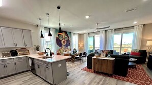 Une cuisine moderne avec des meubles gris, un îlot central, des luminaires suspendus et un coin repas avec une nappe à carreaux.