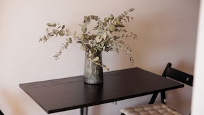 Una mesa de comedor con un jarrón de ramas de eucalipto, dos sillas con asientos acolchados y una superficie de mesa de madera oscura.