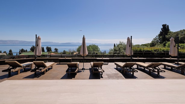 Terraza con tumbonas y sombrillas con vista a un cuerpo de agua y montañas.
