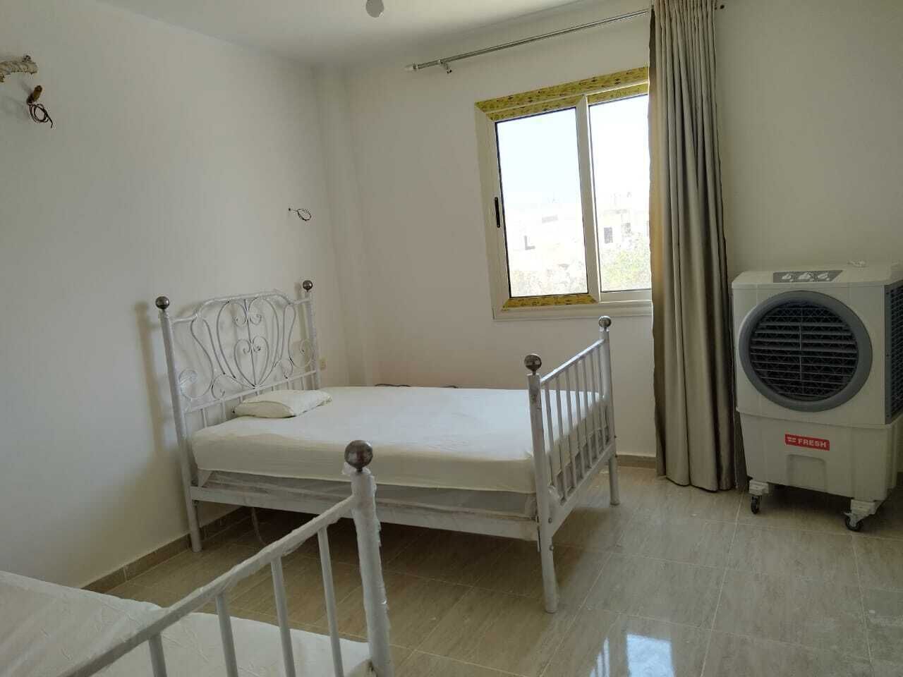 Een kamer met een enkel bed, een raam met gordijnen en een staande airconditioning.