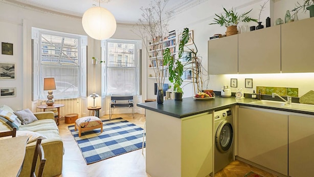 En modern lägenhet med kök, matplats och vardagsrum. Den är utrustad med tvättmaskin, ett matbord med stolar, en soffa och ett stort fönster med utsikt över staden.