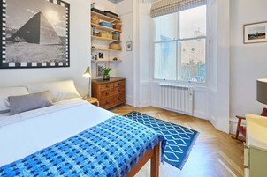 Un dormitorio con cama, cómoda, ventana con vistas y estantería con cajas de almacenamiento.