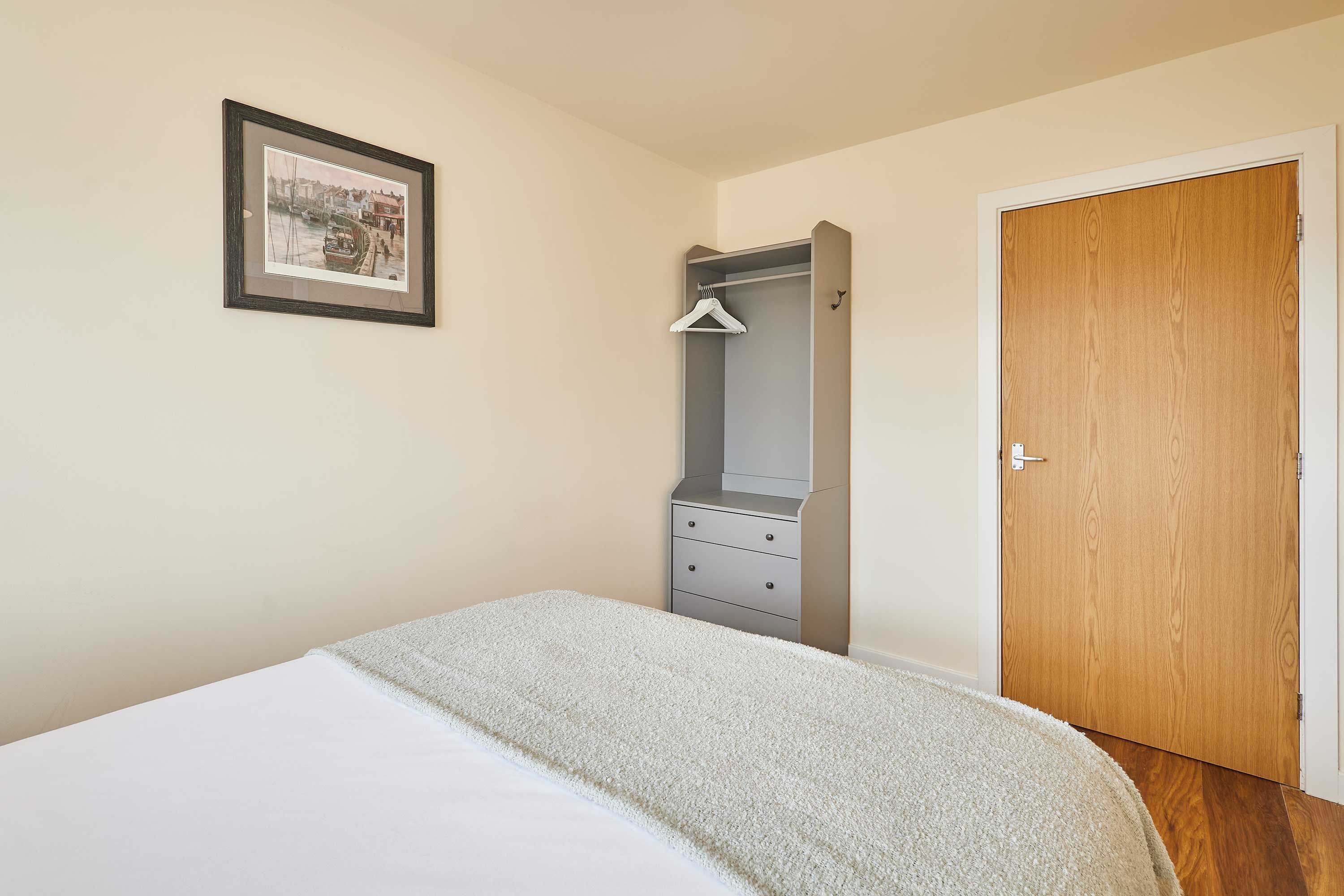 A bedroom with a bed, a wardrobe, a door, and a framed picture on the wall.