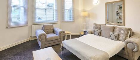 A hotel room with a bed, two armchairs, a small table, and a lamp.