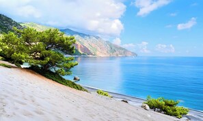 A beach with a clear view of the sea and a mountain in the background.