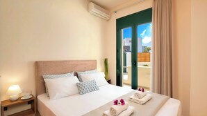 A hotel room with a bed, a nightstand, a lamp, and a view of the outside. - Eliomar Beachside Villa (Chania)