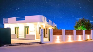 A modern two-story house with a flat roof, large windows, and a well-lit entrance. - Eliomar Beachside Villa (Chania)