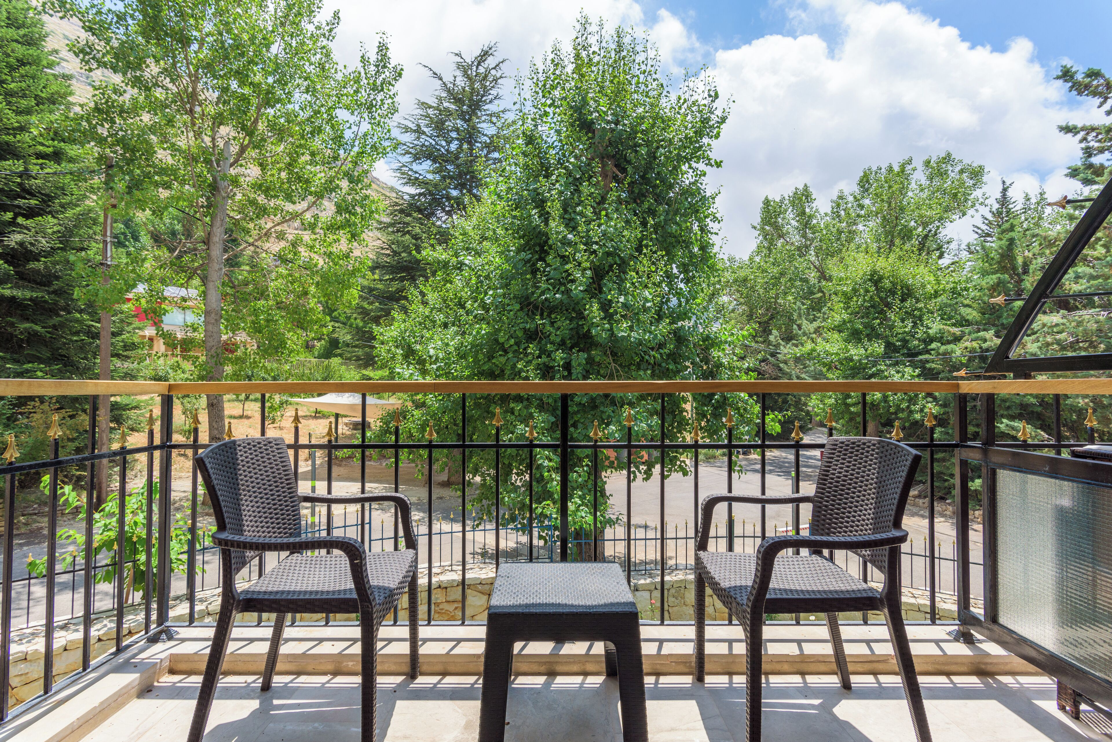 Un balcone con due poltrone in vimini e un tavolino, con vista su un'area parcheggio e alberi.