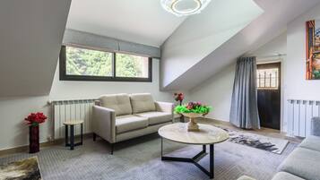 A modern living room with a sofa, a coffee table, and a view of the outdoors through a large window.