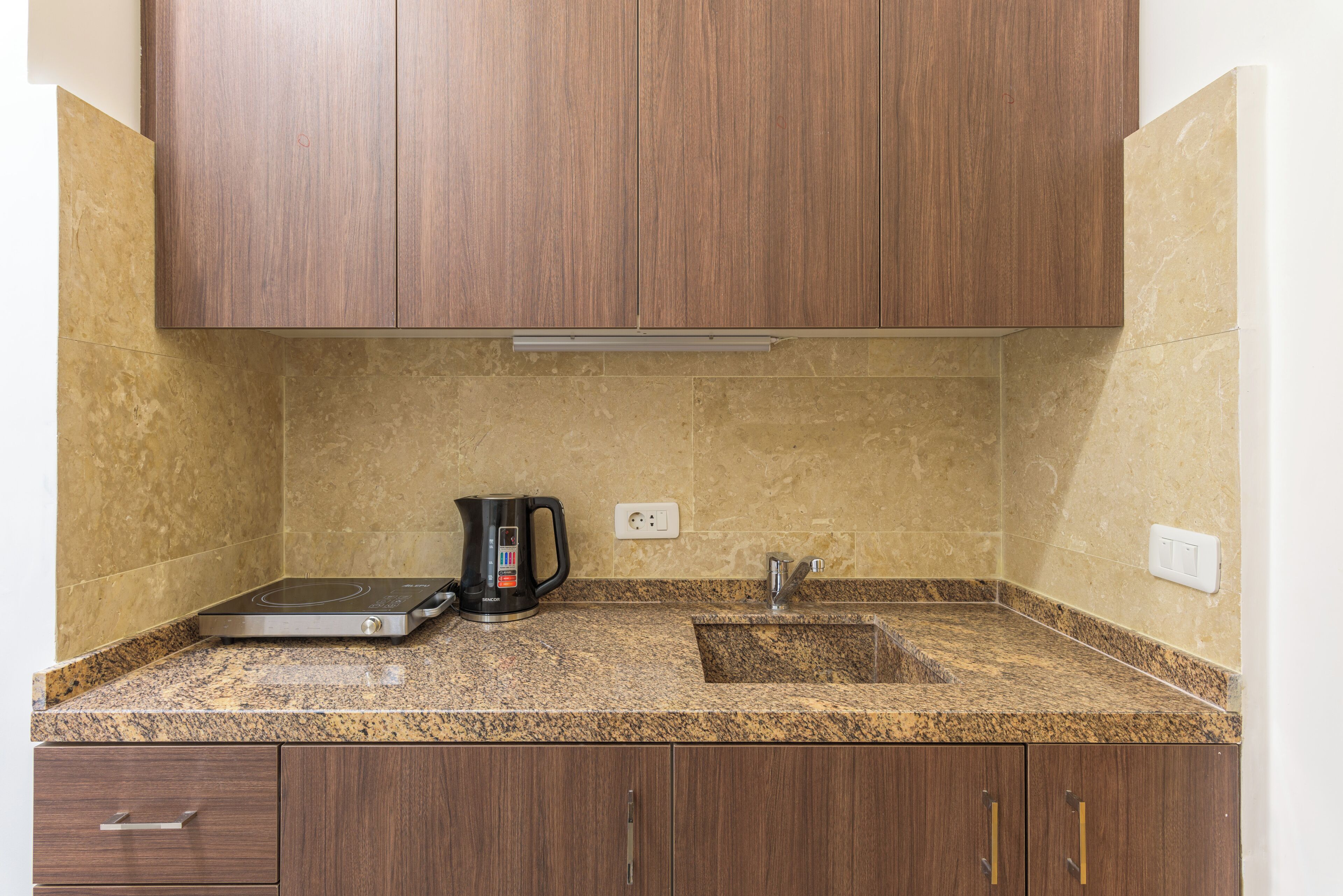 A kitchen with granite countertops, a built-in electric kettle, and wooden cabinets.