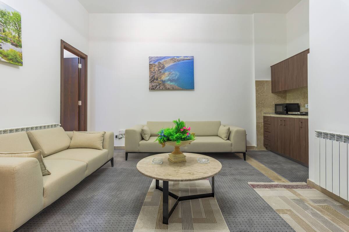 A living room with two sofas, a coffee table, and a painting of a coastal scene.