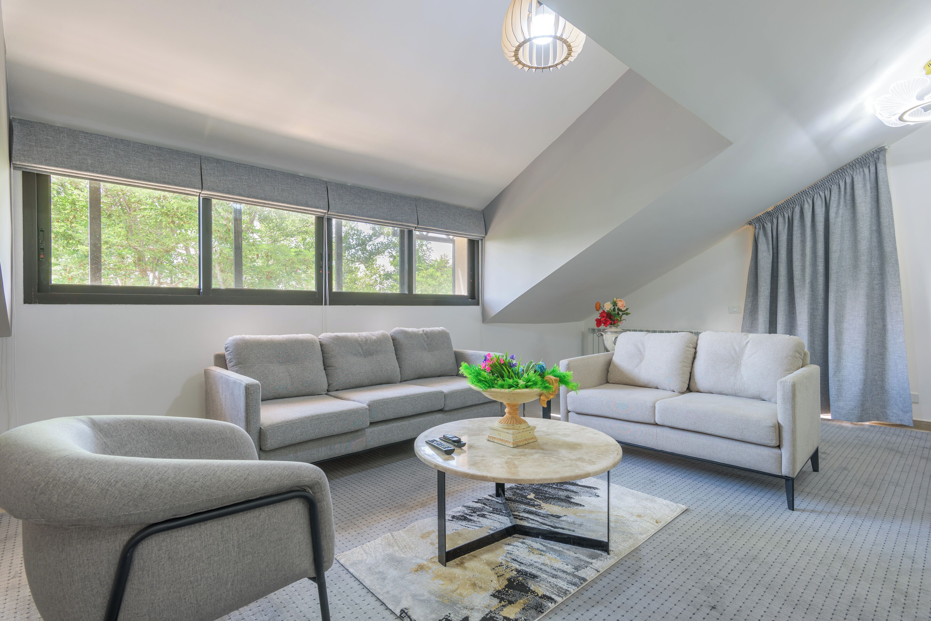 Een moderne woonkamer met een grijze bank, een ronde salontafel en een groot raam met gordijnen.