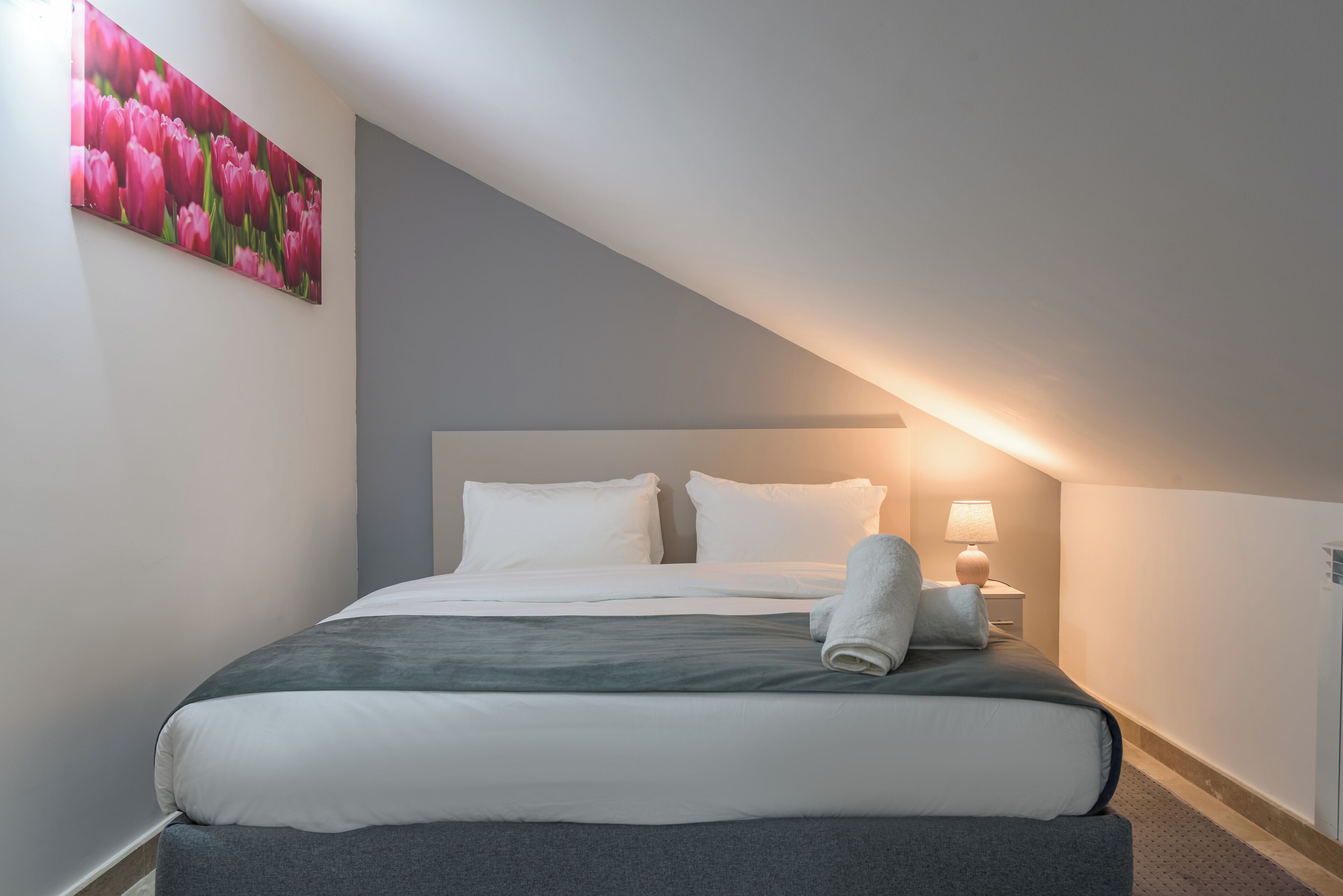 A neatly made bed with white and grey bedding, a single pillow, and a folded towel on the side.