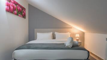 A neatly made bed with white and grey bedding, a single pillow, and a folded towel on the side.