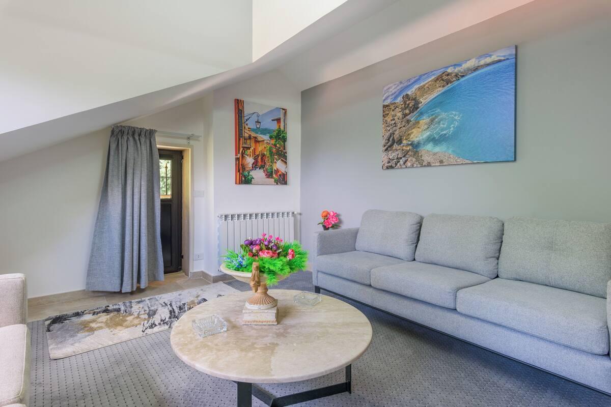 A modern living room with a grey sofa, a round coffee table, and a painting of a coastal scene.
