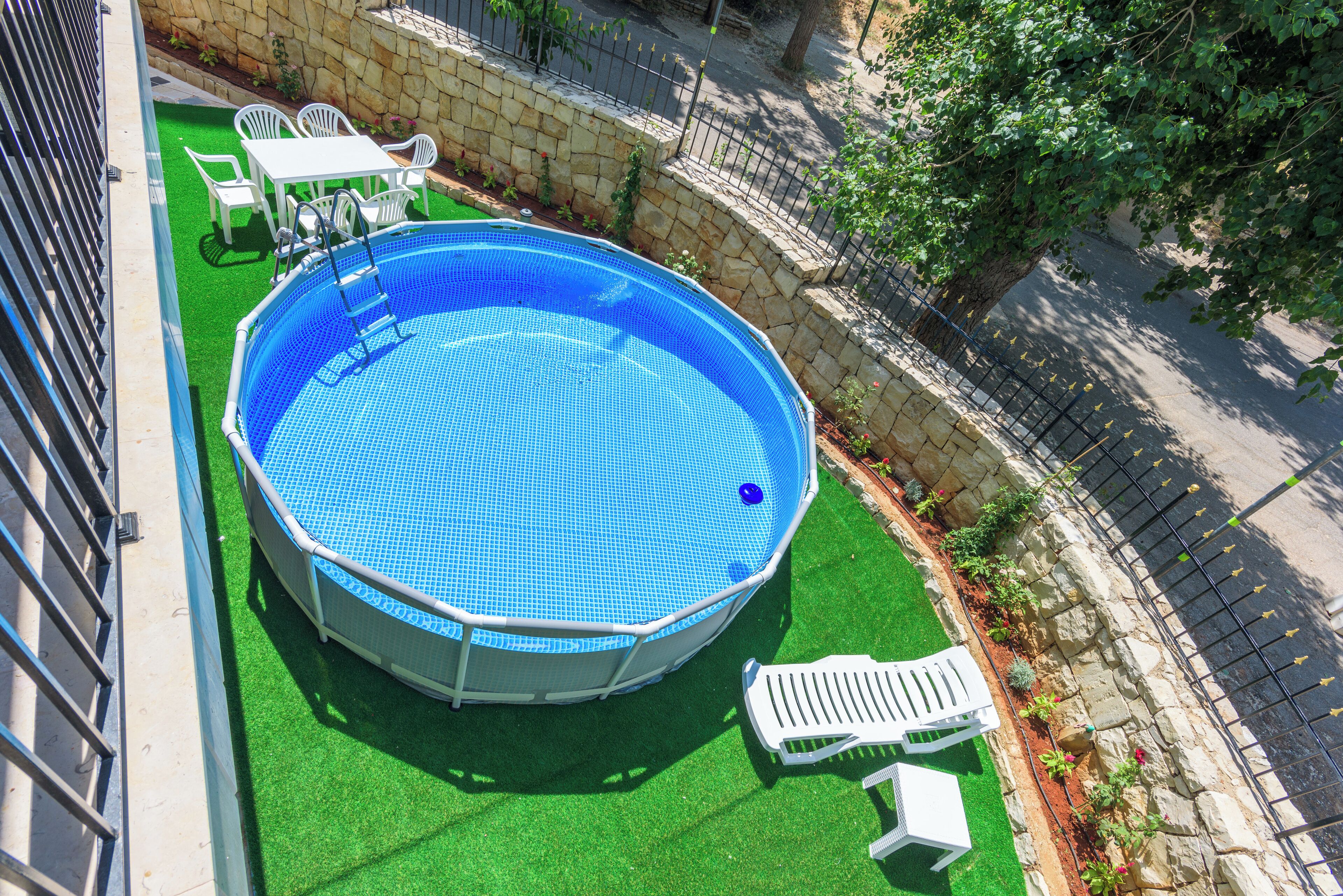 A round above-ground pool with a blue tiled surface, surrounded by artificial green turf and white plastic chairs.