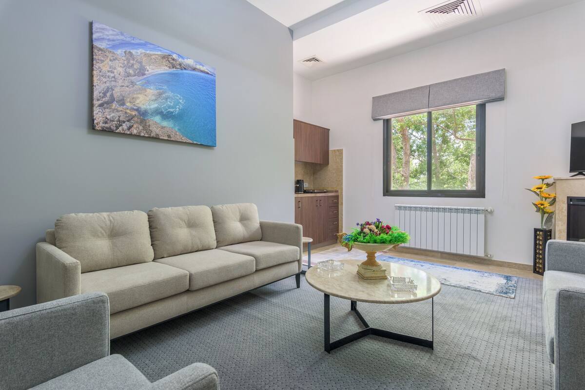 A modern living room with a beige sofa, a coffee table with a vase, and a painting of a coastal scene.