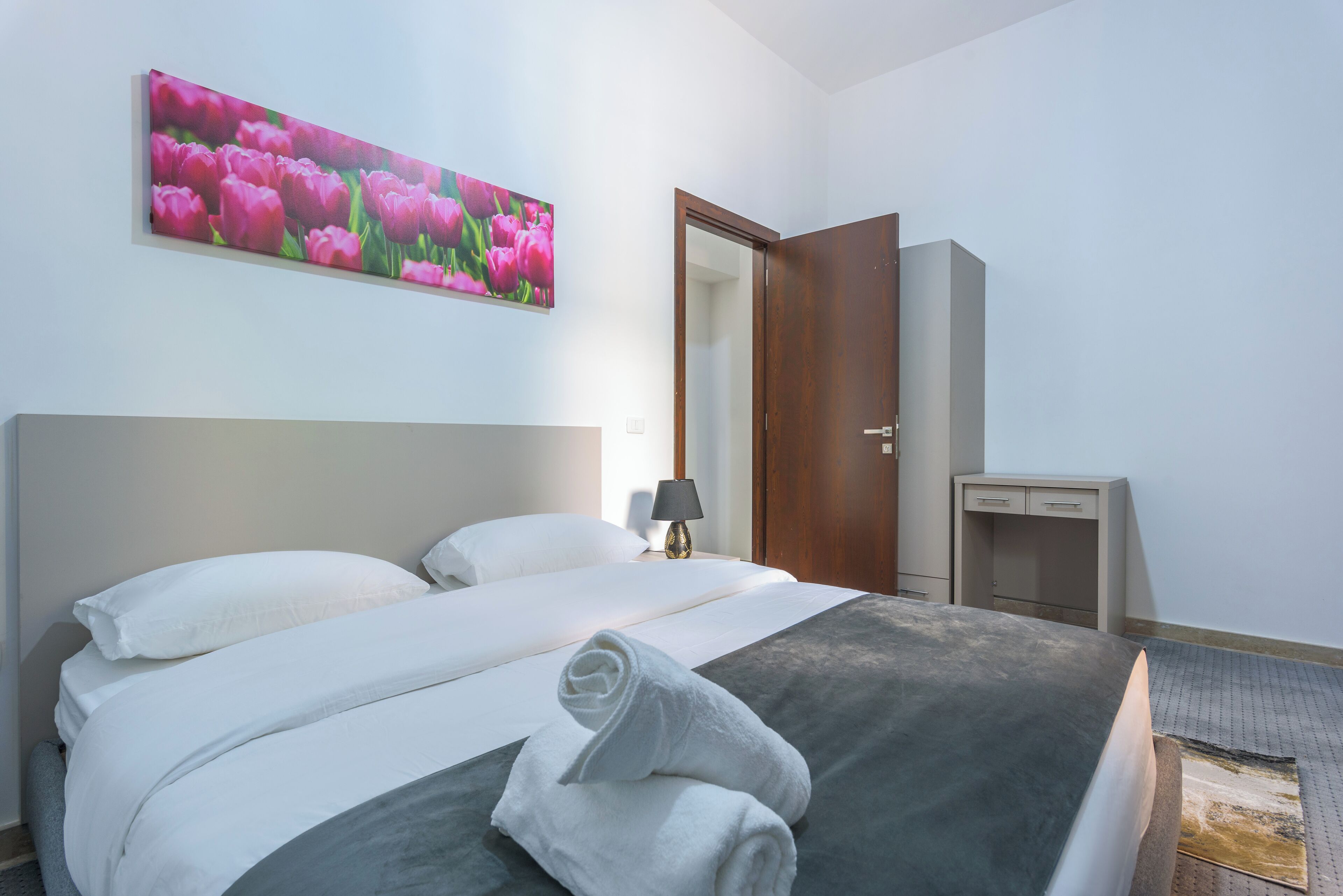 Una habitació d'hotel amb un llit gran, una nit falda amb una làmpada, una porta de fusta i un escriptori petit.