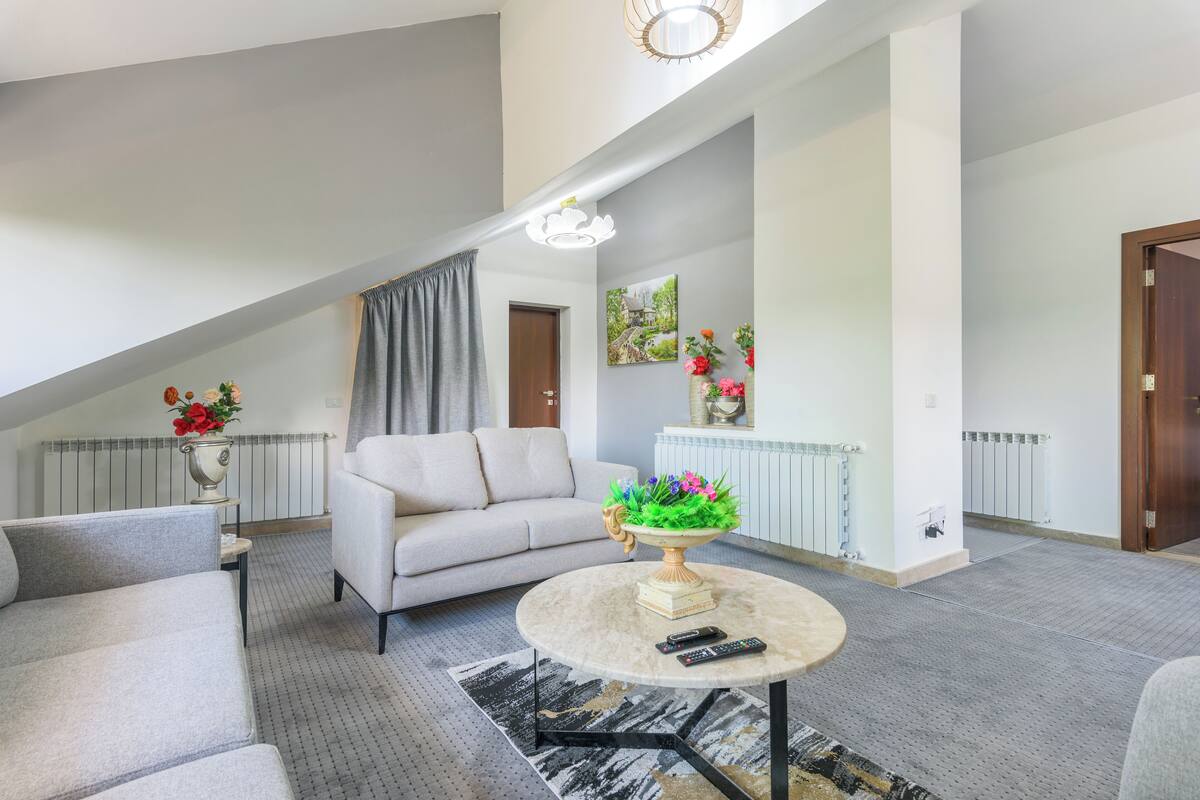 A modern living room with a sofa, a round coffee table with a vase of flowers, and a ceiling light fixture.