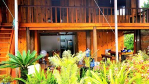 A wooden cabin with a balcony, a dining area with outdoor furniture, and lush greenery. - Thanh Binh Homestay Mang Den TT Mang Den (Mang Den)