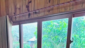 A room with wooden paneled walls and large windows offering a view of greenery and a distant building. - Thanh Binh Homestay Mang Den TT Mang Den (Mang Den)