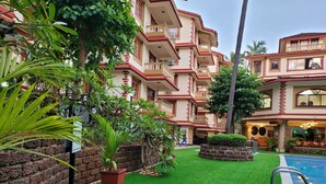 Un patio de hotel con césped artificial, piscina y un edificio de varios pisos con balcones.