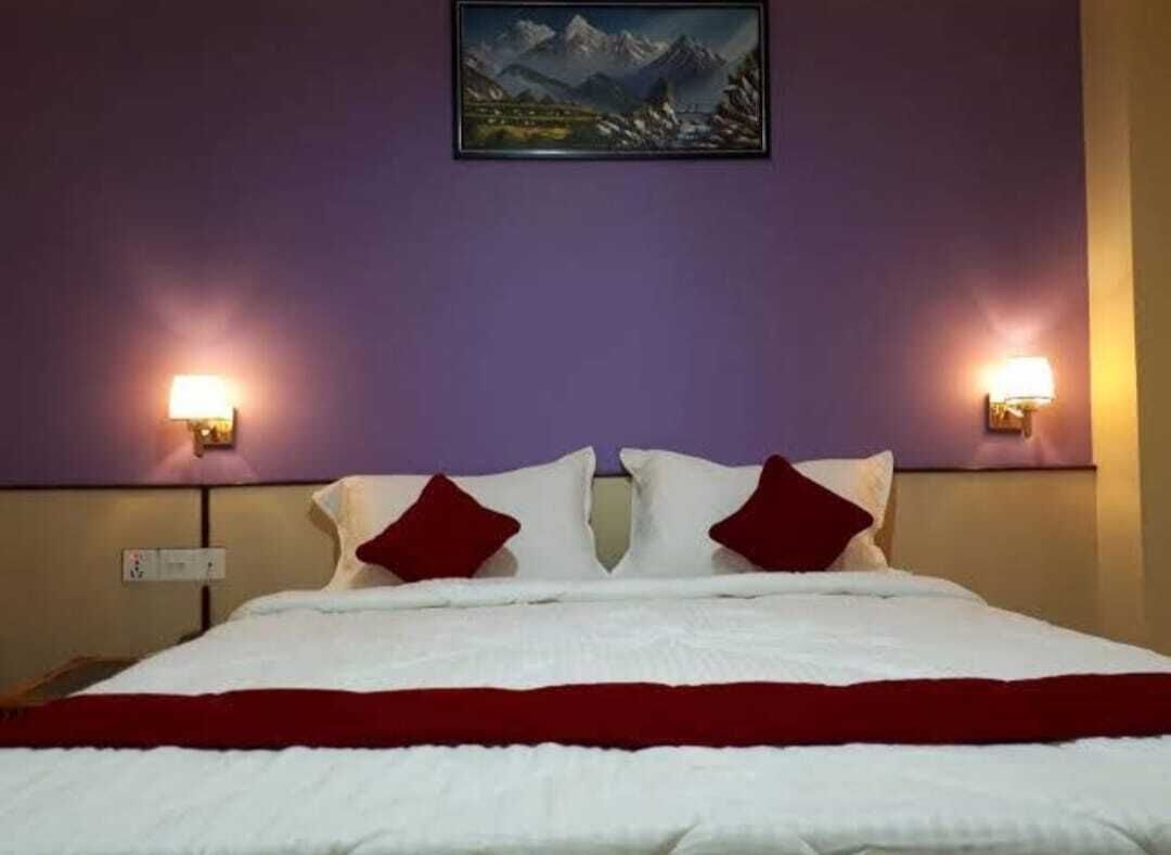 Una habitación de hotel con una cama, dos lámparas de pared y un cuadro con paisaje de montañas en la pared.