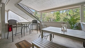 A covered patio with a table and chairs, a lantern, and a view of trees through the windows. - Memories are Made Here (Hilton Head Island)