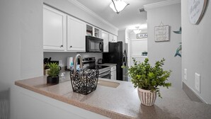 A modern kitchen with white cabinetry, a granite countertop, a black refrigerator, a microwave, and a sink. There are two potted plants on the counter. - Memories are Made Here (Hilton Head Island)