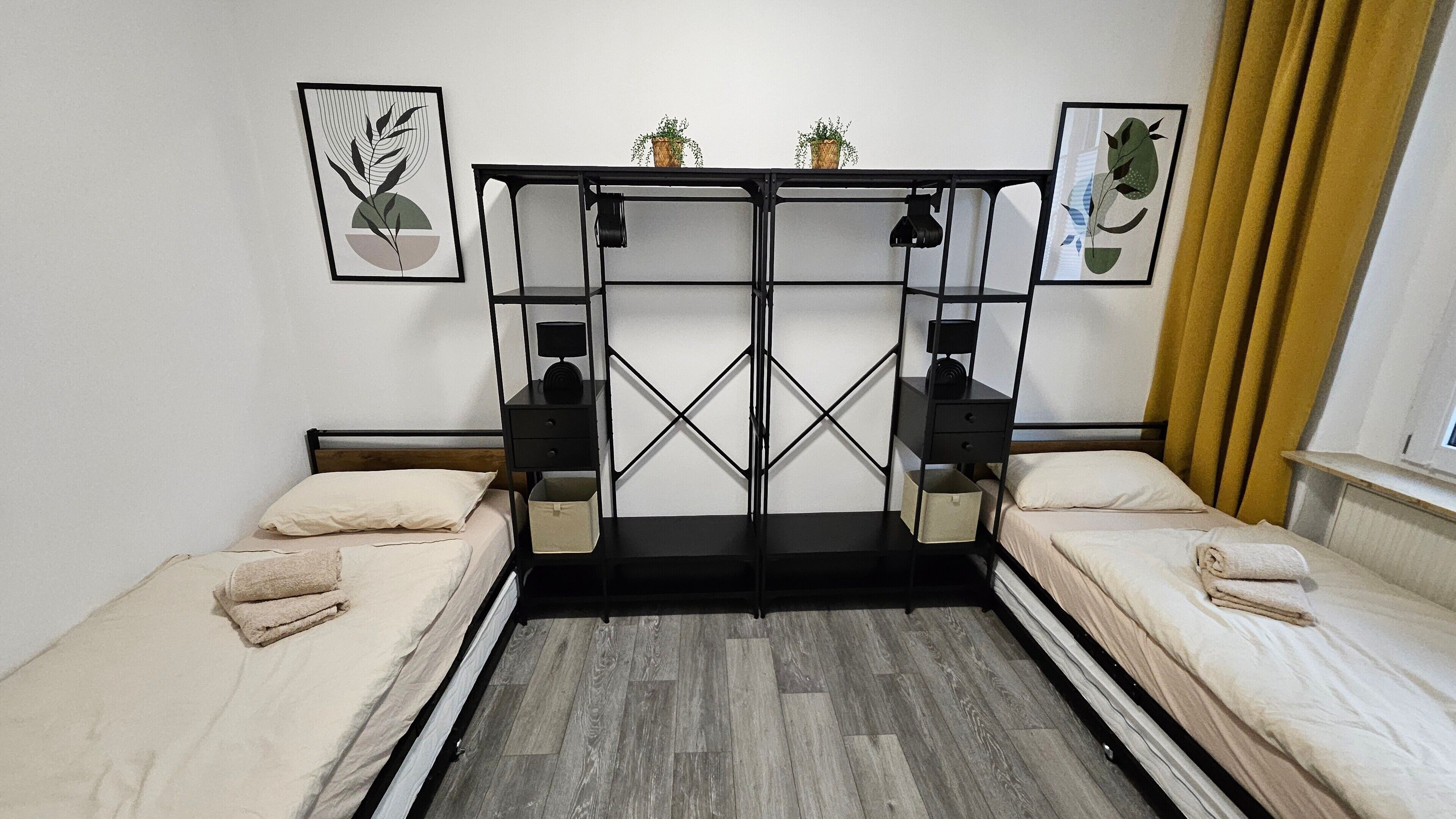 Una habitación con dos camas, una mesa central con una lámpara y dos cuadros en la pared.