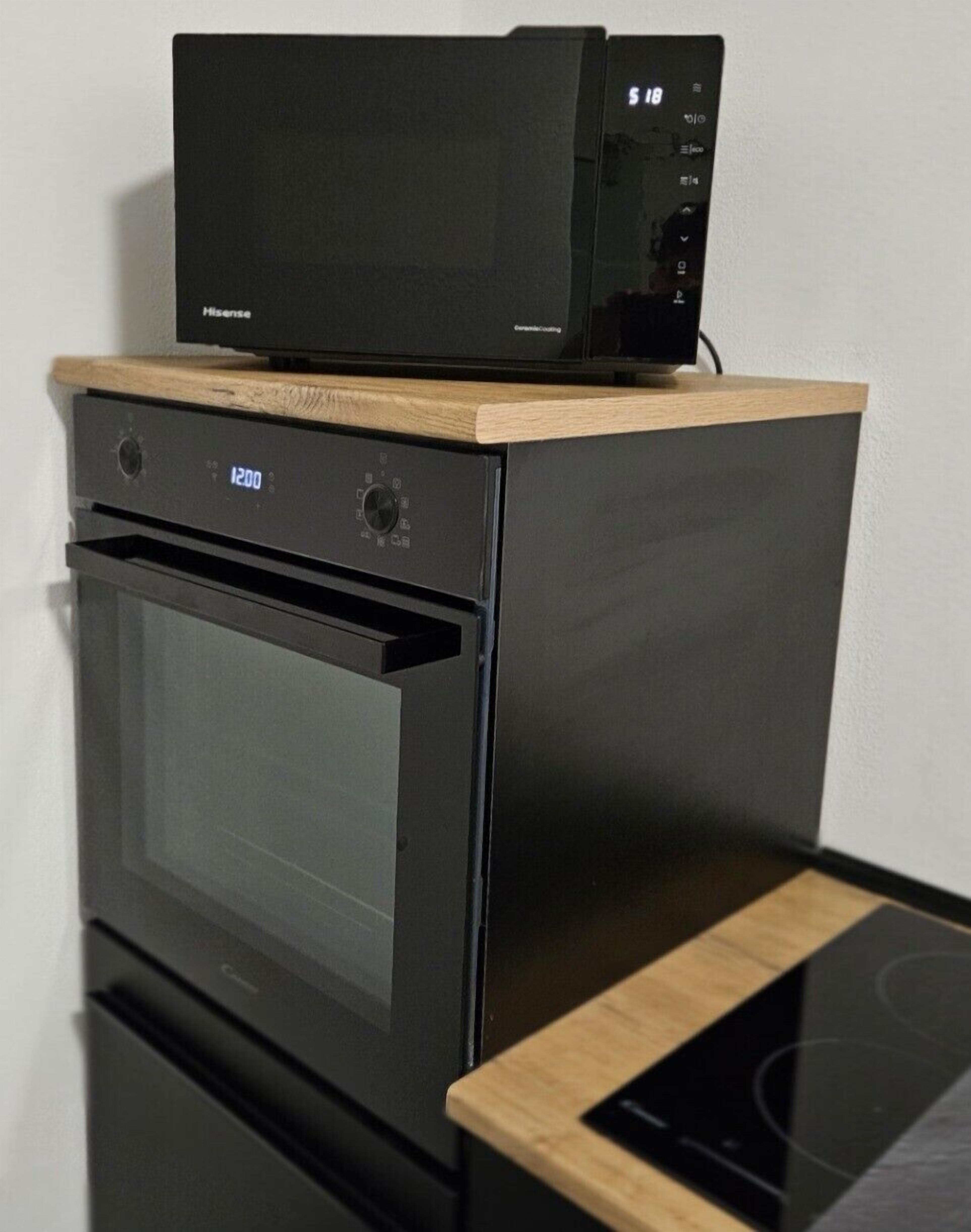 A compact kitchen with a microwave on top of a built-in oven, a stovetop, and a wooden countertop.
